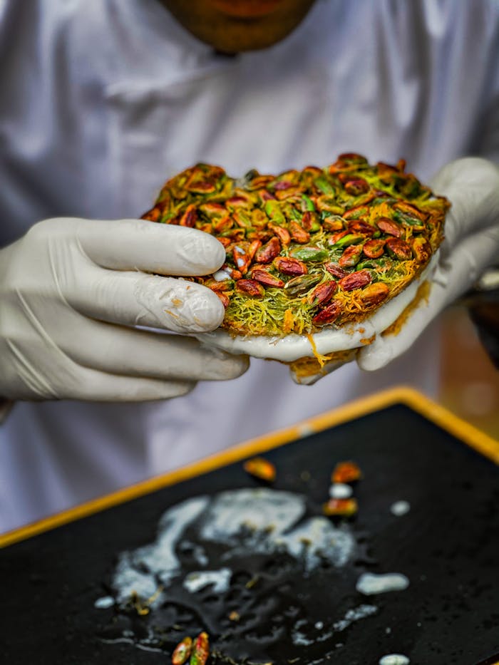 Close-up of traditional kunafa dessert topped with pistachios, being served by a chef.